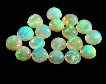 May include: A selection of polished opal gemstones, each with a rounded cabochon shape. The opals have a milky white base colour with flashes of iridescent colour, including green, orange, and blue, against a black background.