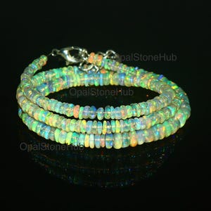 Puede incluir: Un collar de múltiples hilos hecho de cuentas de ópalo iridiscente. Las cuentas son una mezcla de colores verde claro, blanco y amarillo. El collar está enhebrado en una cadena de plata.