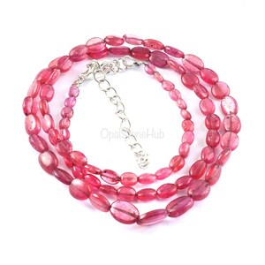 May include: A pink gemstone necklace with oval-shaped beads. The necklace is made of multiple strands of beads and has a silver clasp.
