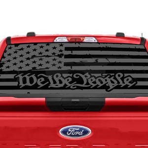 May include: A red pickup truck with a black and white American flag decal on the rear window. The decal features the words "We the People" in a stylized font.