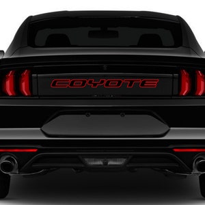 May include: Black Ford Mustang with red taillights and a red "COYOTE" decal on the rear window.