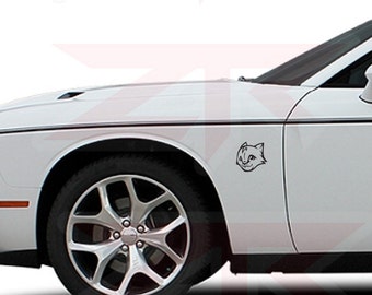 May include: A white car with a black cat face decal on the front fender. The car has black accents along the side and a black rim on the front tire.
