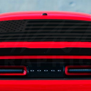 May include: A red Dodge Challenger with a black American flag decal on the rear window. The decal is a silhouette of the American flag with white stars and red and white stripes.