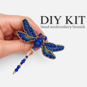 May include: A DIY kit for a bead embroidery brooch shaped like a dragonfly. The brooch features deep blue and gold beads, a central blue crystal, and a long tail made of blue and translucent beads. The text DIY KIT bead embroidery brooch is visible.