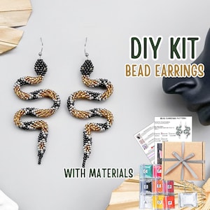 May include: DIY bead earring kit with materials. The earrings are in the shape of a snake, with black, gold, and white beads. The kit includes a pattern, beads, and other supplies. The text "DIY KIT BEAD EARRINGS WITH MATERIALS" is visible.