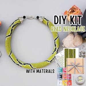 May include: A DIY bead necklace kit featuring a lime green, black, and white patterned beaded rope necklace with silver-toned metal clasps. The kit includes a printed pattern guide, small bags of coloured beads, needles, and a spool of thread in a box.