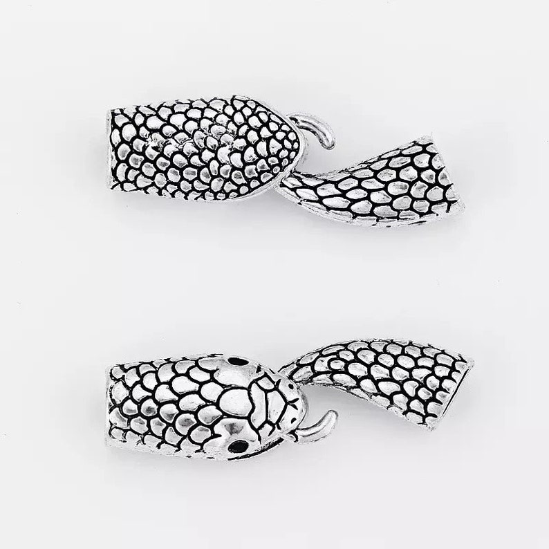 Peut inclure: Deux fermoirs &agrave; glissi&egrave;re en forme de serpent argent&eacute;s avec un motif textur&eacute; et &eacute;cailleux. Les fermoirs sont con&ccedil;us pour &ecirc;tre utilis&eacute;s comme fermeture pour des colliers, des bracelets ou d'autres bijoux.