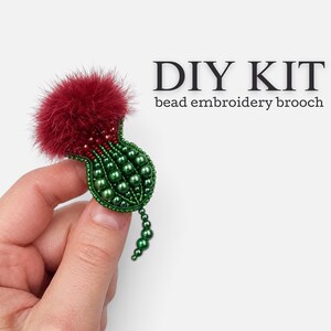 May include: A DIY kit for a bead embroidery brooch shaped like a thistle. The brooch features a fluffy deep red top and a green base constructed from various sizes of green beads. The text DIY KIT bead embroidery brooch is visible.