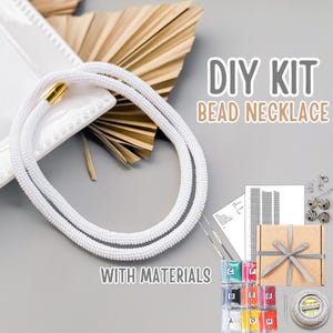 Peut inclure: Un collier de perles blanches avec un fermoir doré est présenté avec un kit de bricolage. Le kit comprend des perles de différentes couleurs, des outils et une boîte cadeau nouée avec un ruban gris. Le texte sur l'image indique "DIY KIT BEAD NECKLACE WITH MATERIALS."