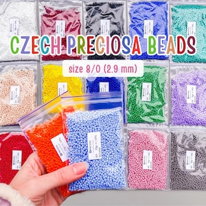 Puede incluir: Una colección de cuentas checas Preciosa en varios colores, empaquetadas en bolsas de plástico transparente. Las cuentas son de tamaño 8/0 (2,9 mm). El texto "CZECH PRECIOSA BEADS" es visible.