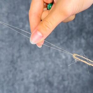 May include: Close-up of a hand holding two strands of white thread, connected to a bundle of brown twine. The background is a mottled gray. The image highlights the contrast between the delicate thread and the rustic twine.