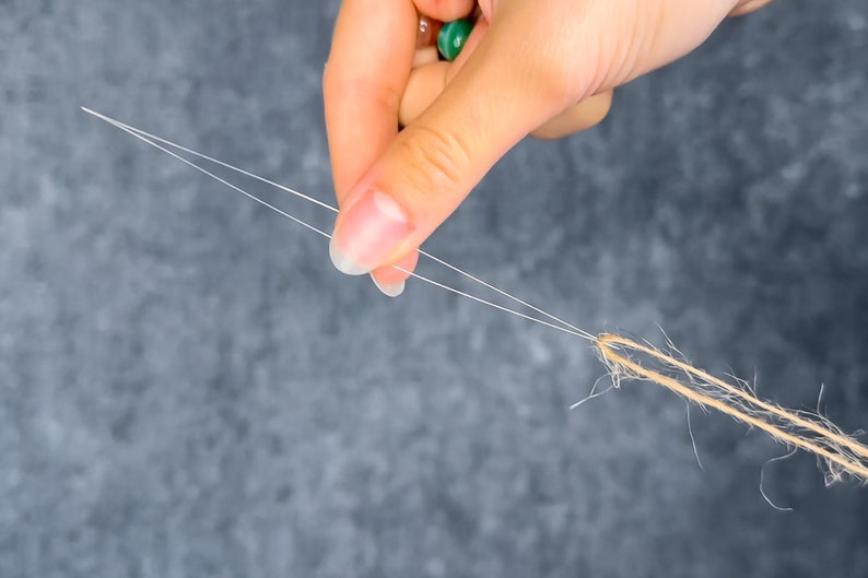 May include: Close-up of a hand holding two strands of white thread, connected to a bundle of brown twine. The background is a mottled gray. The image highlights the contrast between the delicate thread and the rustic twine.