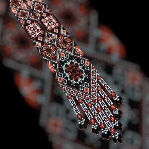 Op de afbeelding: Een paar lange, kralenkettingen met zwarte, witte en oranje geometrische patronen. De kettingen hebben franjes aan de onderkant.