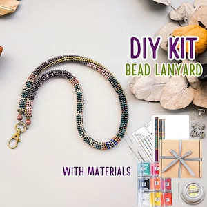 Op de afbeelding: Een doe-het-zelf kralen lanyard kit met materialen. De lanyard is een veelkleurig kralenontwerp met een goudkleurige sluiting. De kit bevat kralen, draad, een geschenkdoos en instructies. De tekst op de afbeelding luidt "DIY KIT BEAD LANYARD WITH MATERIALS."