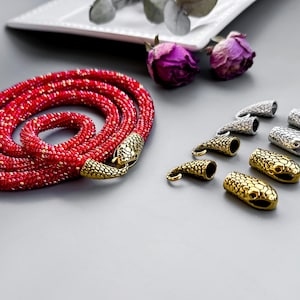 Peut inclure: Un collier de perles rouges avec des fermoirs en forme de serpent. Le collier est enroul&eacute; sur une surface grise. Il y a aussi plusieurs fermoirs en forme de serpent argent&eacute;s et dor&eacute;s sur la surface.