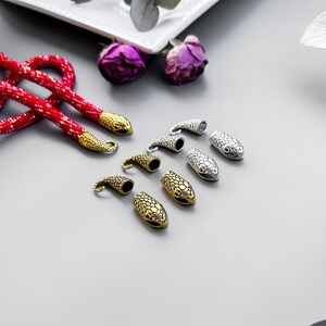 Peut inclure: Un collier de perles rouges avec des embouts en forme de serpent dor&eacute;s et argent&eacute;s. Les embouts ont un design textur&eacute; et &eacute;cailleux.