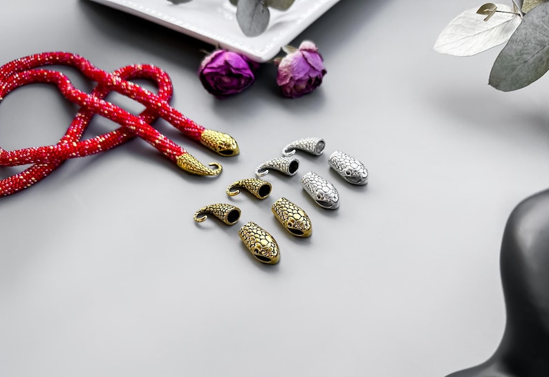 Peut inclure: Un collier de perles rouges avec des embouts en forme de serpent dor&eacute;s et argent&eacute;s. Les embouts ont un design textur&eacute; et &eacute;cailleux.