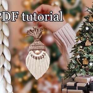 Peut inclure: Une décoration de gnome en fil blanc avec un chapeau en feutre marron et un nez en perle de bois. Le gnome est suspendu à un sapin de Noël décoré de maisons en bois, de pommes de pin et d'étoiles blanches. Le texte "PDF tutorial" est visible sur l'image.