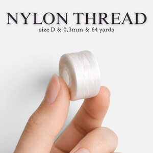 May include: A small spool of white nylon thread with text reading NYLON THREAD, size D & 0.3mm & 64 yards. The thread is wound tightly around a cylindrical core, showing a smooth, consistent texture and a bright, clean white color throughout.