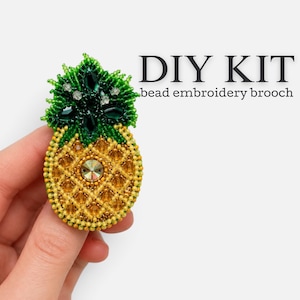 May include: A DIY kit for a bead embroidery brooch shaped like a pineapple. The pineapple features yellow and gold beads for the body with a central crystal, and dark green beads with faceted stones for the leaves. The text reads DIY KIT.