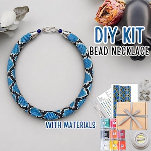 May include: A DIY bead necklace kit featuring a circular necklace with a blue, black, and white geometric pattern. The kit includes a cardboard box with a ribbon, printed instruction sheets, needles, and small bags of coloured beads for assembly.