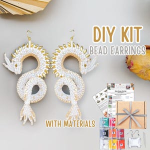 Könnte beinhalten: DIY-Kit für weiße und goldfarbene Perlen-Drachenohrringe. Die Ohrringe sind in Drachenform, mit weißen Perlen und goldenen Akzenten. Das Set enthält Materialien und Anleitungen. Der Text auf dem Bild lautet "DIY KIT BEAD EARRINGS WITH MATERIALS".