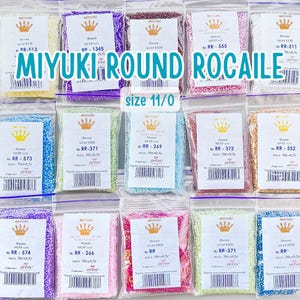 May include: A collection of small, round, colorful beads in clear plastic bags. Each bag has a label with the brand name "MIYUKI" and the bead size "11/0". The bags are arranged in a grid pattern.