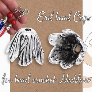 May include: Two silver end bead caps for bead crochet necklaces. The caps have a flower-like design with a hole in the centre.