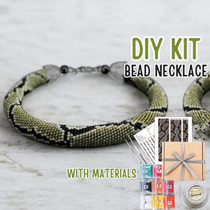 May include: DIY bead necklace kit with materials. The kit includes a beaded necklace with a snake-like pattern in green, black, and white. The kit also includes beads, needles, and a gift box with a gray ribbon.