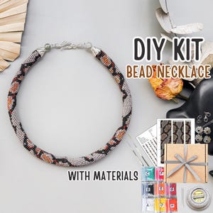 Peut inclure: Un kit de collier de perles à faire soi-même avec du matériel. Le collier est de forme circulaire avec un motif de perles grises, noires, oranges et rouges. Le kit comprend des perles, des aiguilles, du fil et un patron. Le texte "DIY KIT BEAD NECKLACE WITH MATERIALS" est visible.
