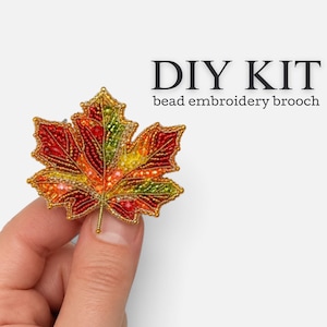 Peut inclure: Un kit de broderie de perles DIY en forme de feuille d'érable avec un dégradé de perles en verre rouges, orange, jaunes et vertes. Le texte DIY KIT bead embroidery brooch est imprimé en noir sur le côté droit du motif de la feuille.