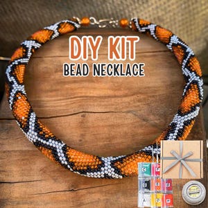 Può includere: Kit fai-da-te per una collana di perline con un motivo a pelle di serpente. Il kit include perline di vari colori, filo e istruzioni. La collana è arancione, nera e bianca.