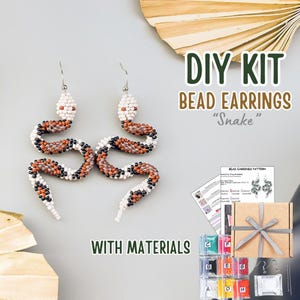 Peut inclure: Un kit de bricolage pour fabriquer des boucles d'oreilles serpent en perles. Les boucles d'oreilles sont blanches, noires et marron. Le kit comprend des perles, des instructions et d'autres matériaux. Le texte dit "DIY KIT BEAD EARRINGS Snake WITH MATERIALS."