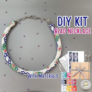 May include: A DIY bead necklace kit featuring a circular beaded necklace with a white base and floral patterns in blue, green, and pink. The kit includes a cardboard box with a ribbon, a printed pattern guide, needles, and small bags of colourful beads.