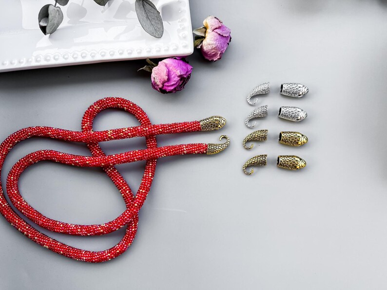 Peut inclure: Un collier de perles rouges avec des embouts en m&eacute;tal dor&eacute; et argent&eacute;. Le collier est dispos&eacute; en forme de c&oelig;ur sur une surface grise.
