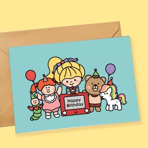May include: A light blue greeting card featuring a cartoon illustration of a group of characters including a child with blonde hair, a brown bear, a green caterpillar, and a unicorn, all wearing party hats. A red toy screen displays Happy Birthday.