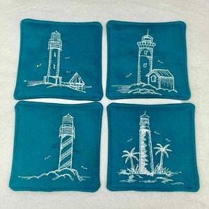 May include: Set of four teal blue square fabric coasters with white embroidered lighthouse designs. Each coaster features a different lighthouse design.