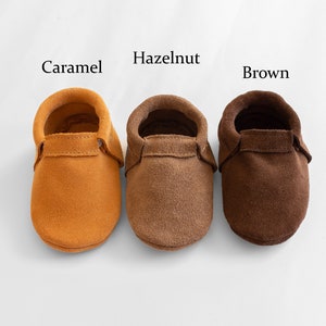 May include: Three pairs of suede baby moccasins in caramel, hazelnut, and brown colors.