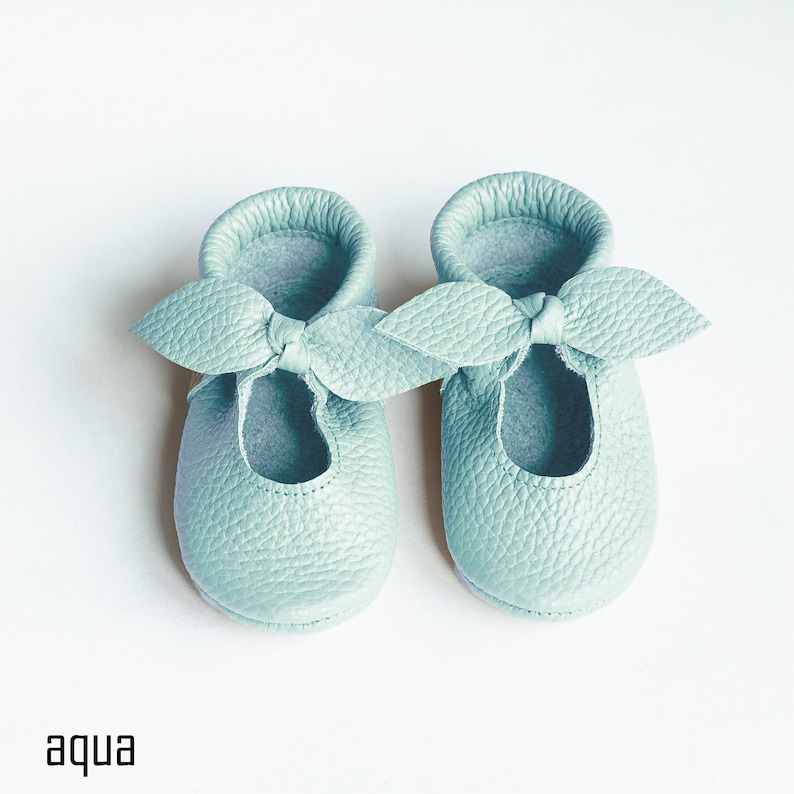 May include: A pair of light blue baby shoes with a bow detail. The shoes are made of soft leather and have a comfortable fit.