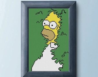 May include: Framed cross-stitch art featuring Homer Simpson from The Simpsons. The artwork depicts Homer's face and upper body against a green background, with a pixelated aesthetic. The frame is a dark gray color.