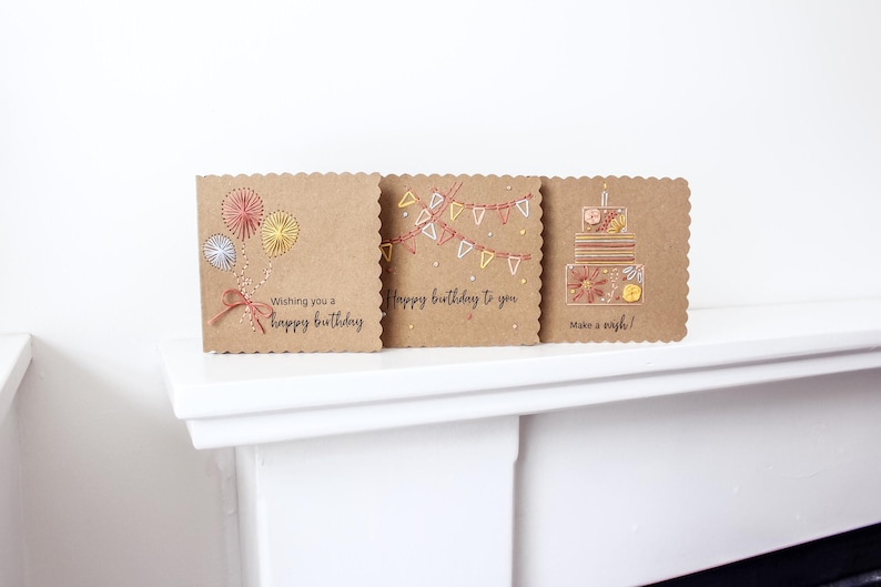 May include: Three birthday cards with scalloped edges are displayed. The cards are made of brown cardstock and feature embroidered designs. One card has fireworks, another has a banner, and the last has a cake. Each card has a birthday message.