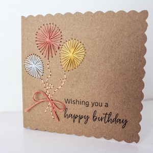 May include: A brown card with a scalloped edge features three colorful balloons made with embroidery floss. The card reads "Wishing you a happy birthday."