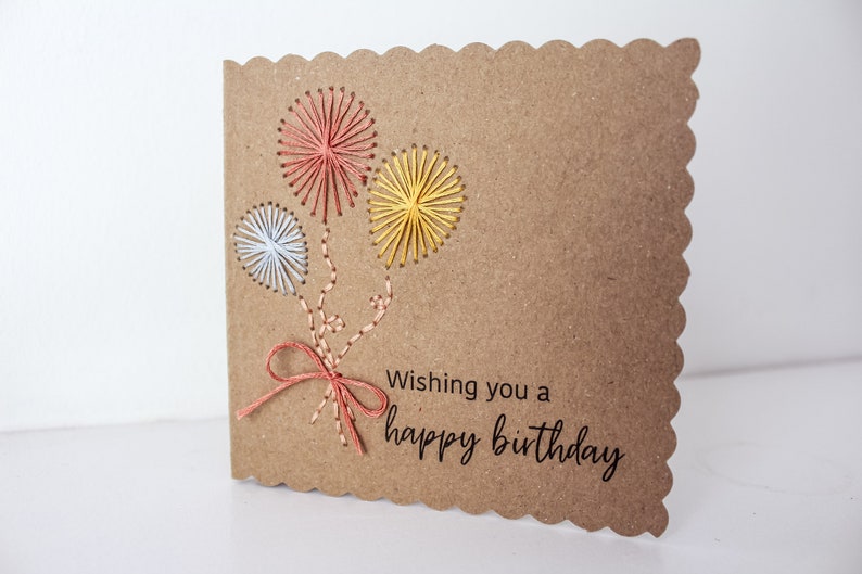 May include: A brown card with a scalloped edge features three colorful balloons made with embroidery floss. The card reads "Wishing you a happy birthday."