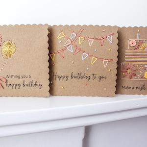 May include: Three handmade birthday cards with scalloped edges. The cards are made of brown cardstock and feature embroidered designs of balloons, bunting, and a cake. Each card has a different birthday message.