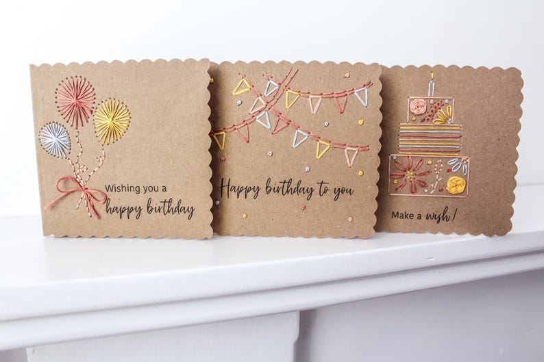 May include: Three handmade birthday cards with scalloped edges. The cards are made of brown cardstock and feature embroidered designs of balloons, bunting, and a cake. Each card has a different birthday message.