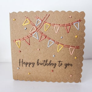 May include: A brown card with a scalloped edge and a hand-stitched design of colorful bunting flags. The card says "Happy birthday to you" in black lettering.