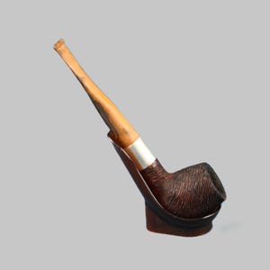 Peut inclure: Une pipe à tabac marron avec un tuyau en bois et un foyer texturé. La pipe a une bague argentée et repose sur un support en bois. Le tuyau est brun clair et le foyer est brun foncé.