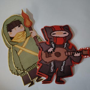 May include: Two cartoon figures are shown. One, in a green hooded cloak, holds a torch. The other, in a red and black outfit, plays a ukulele. Both figures have masked faces and are stylized with bold outlines.