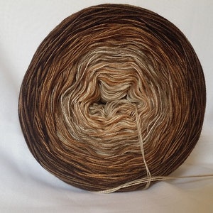 May include: A ball of brown, beige and cream yarn with a gradient effect. The yarn is wound into a circle and is ready to be used for knitting or crocheting.