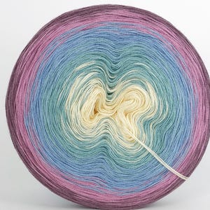 May include: A large ball of yarn in a circular shape, displaying a gradient of colours. The yarn transitions from deep purple to pink, light blue, teal, cream, and back to blue. A single strand of yarn extends from the centre.